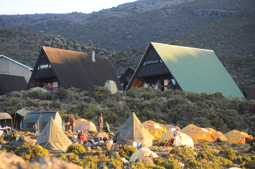 What is the difference between camping and hut accommodation on Kilimanjaro?